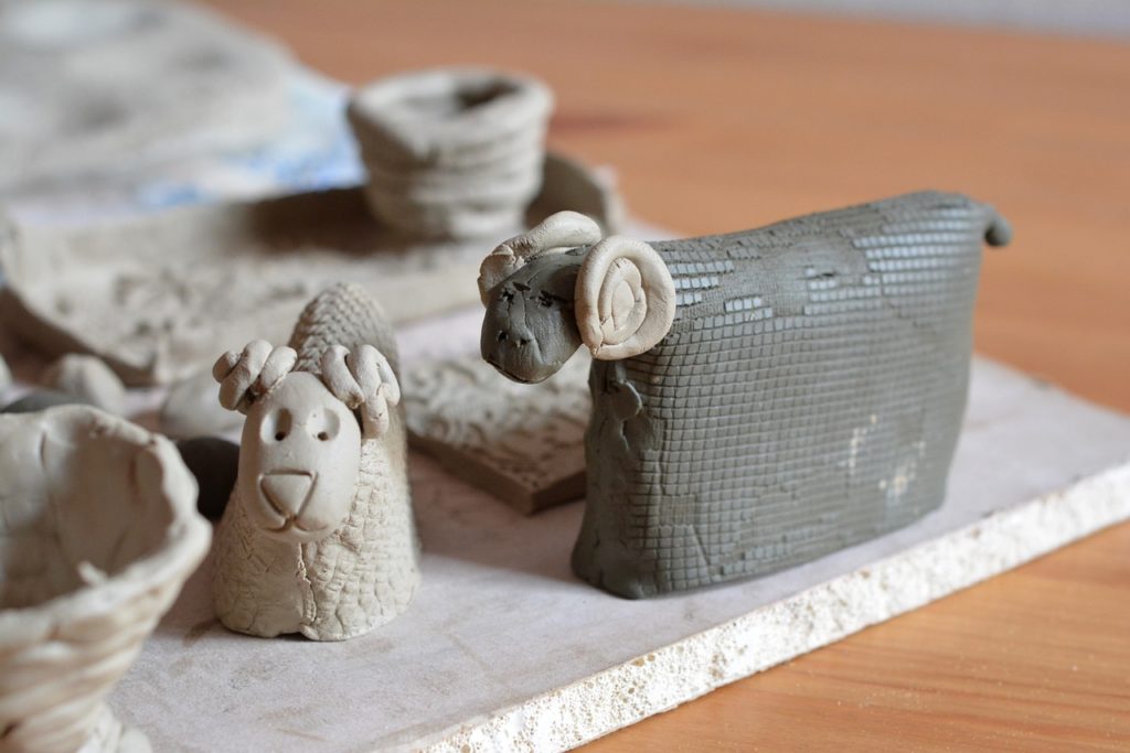 verschiedene ungebrannte Keramikfiguren auf einer weißen Platte: zwei Schafe/Widder, zwei kleine Weidekörbe aus Ton